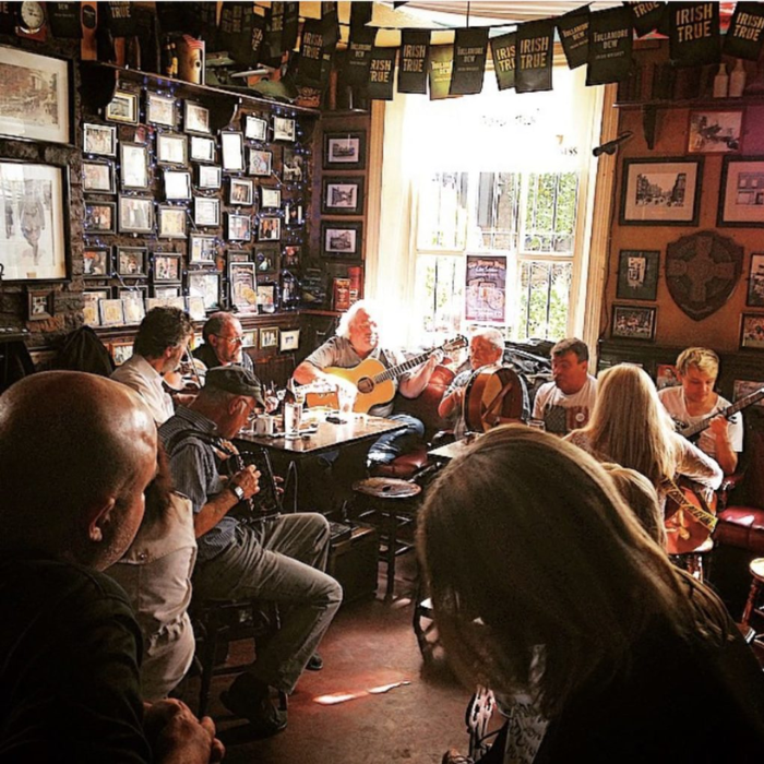 Guests enjoying lively traditional music session in a cosy pub with framed photos on walls, creating an authentic Irish atmosphere.