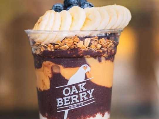 A layered açaí bowl in a clear cup with the Oakberry logo, topped with sliced banana, blueberries, granola, and peanut butter—perfect for celebrating Fathers Day in Dublin.