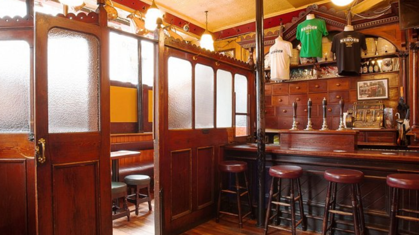 A traditional pub interior with wooden bar stools, ornate woodwork, beer pumps, and frosted glass panels&mdash;perfect for celebrating Fathers' Day in Dublin with branded T-shirts displayed above the bar.
