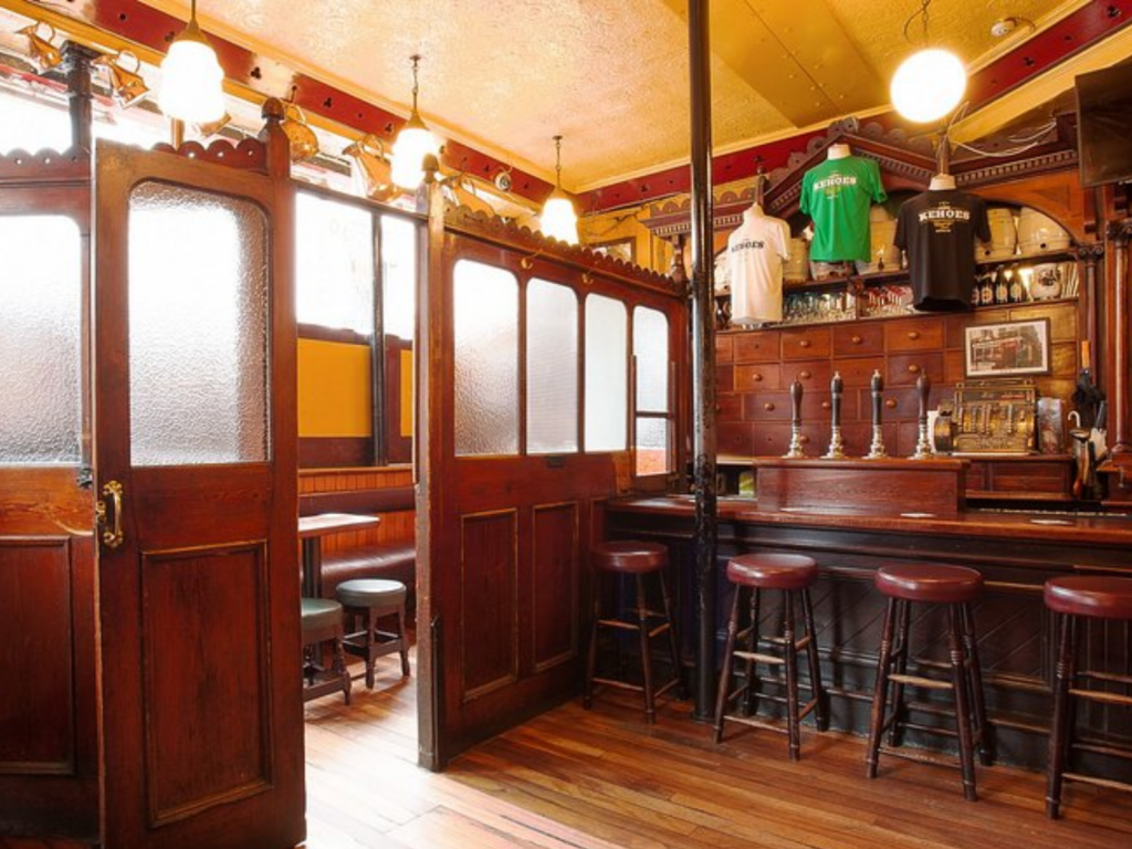 A traditional pub interior with wooden panelling, bar stools, frosted glass partitions, beer taps, and merchandise shirts displayed above the bar—perfect for celebrating Fathers Day in Dublin.