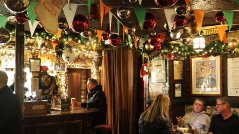 A cosy pub in Dublin, decorated with festive ornaments, garlands, and flags for Fathers’ Day; people sit at tables eating and drinking whilst one person stands at the bar.
