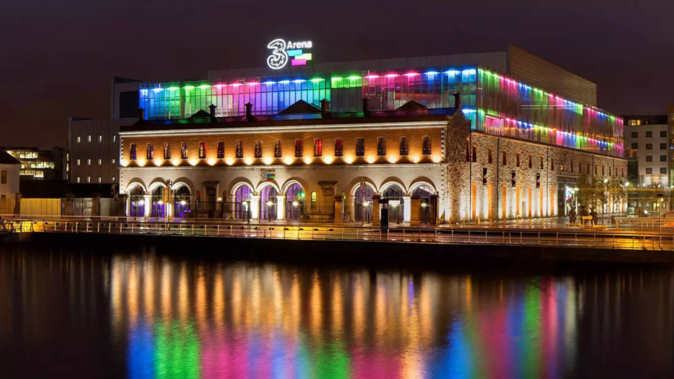 Brightly lit arena with colourful lights reflecting on the water, showcasing vibrant nightlife near the hotel.
